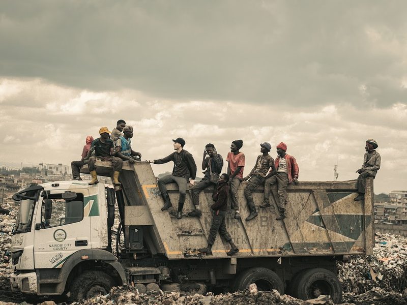 Une dizaine de jeunes assis sur un camion-benne au milieu de la décharge, ciel chargé