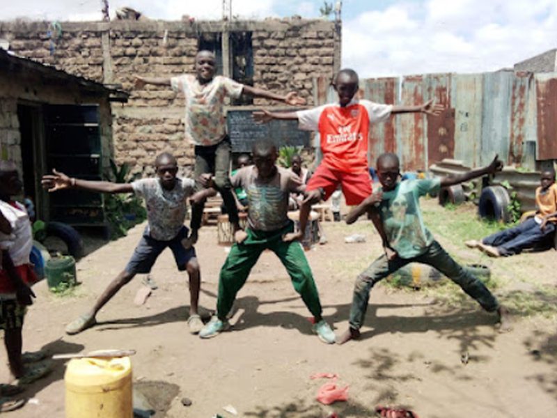 Enfants en pose de danse synchronisée dans une cour en terre, en habits de ville
