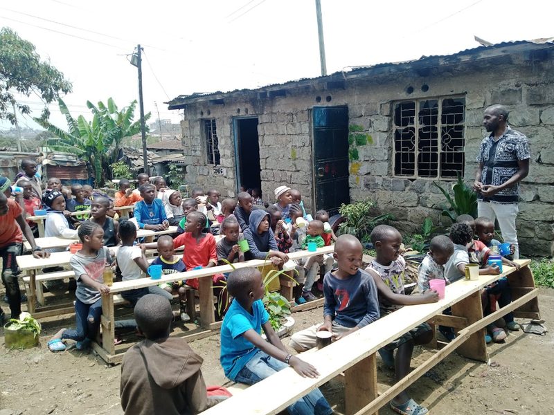 Enfants assis sur de longs bancs en bois autour de tables, en extérieur